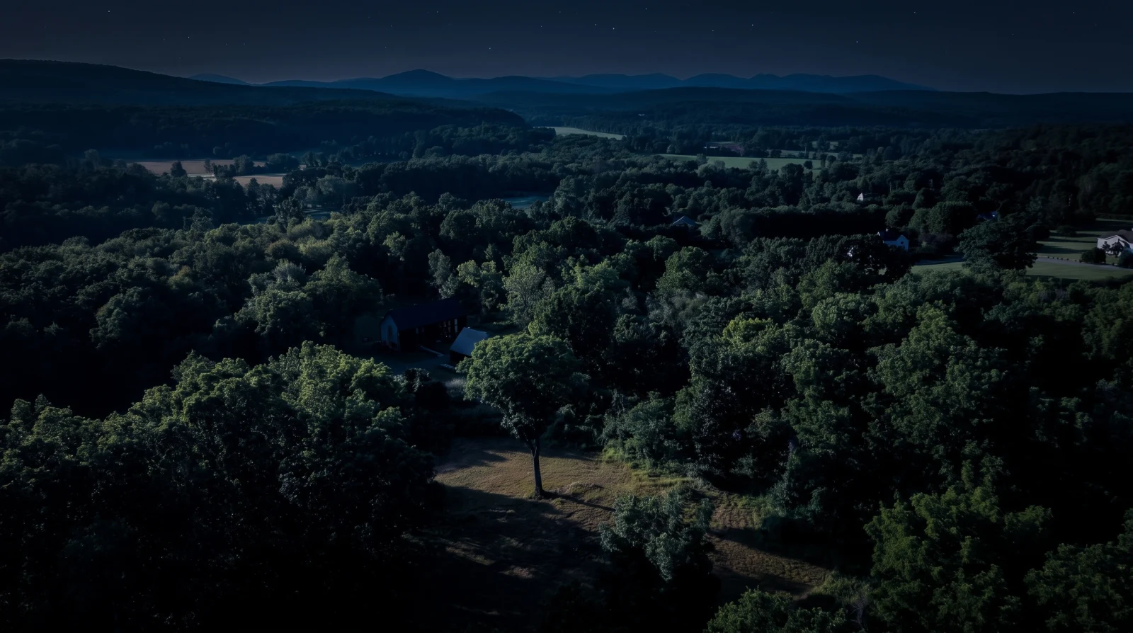Aerial view of the wooded ridge and layered Catskill range at night.
